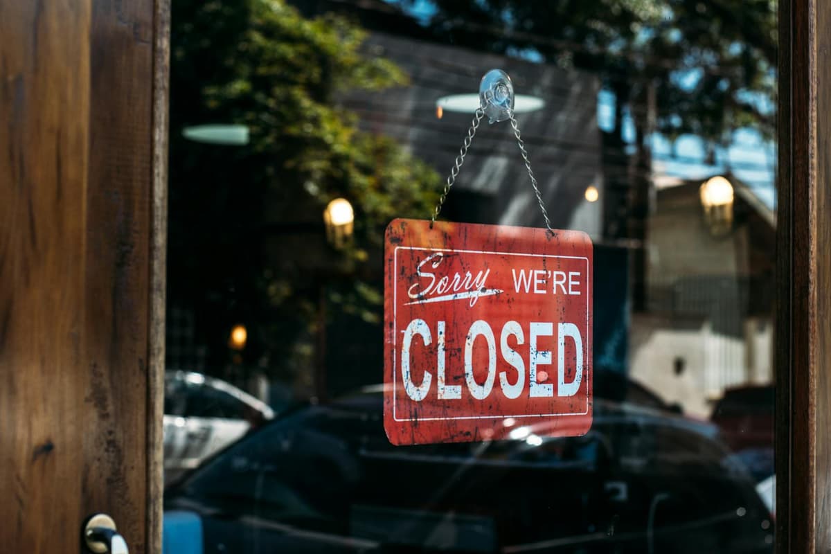 A red closed sign hangs on a glass door, reflecting cars and trees outside.