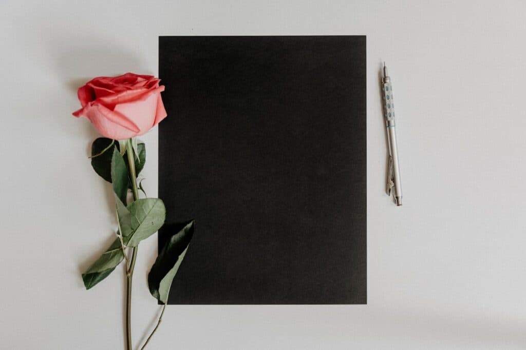 orange rose flower beside notebook and pen