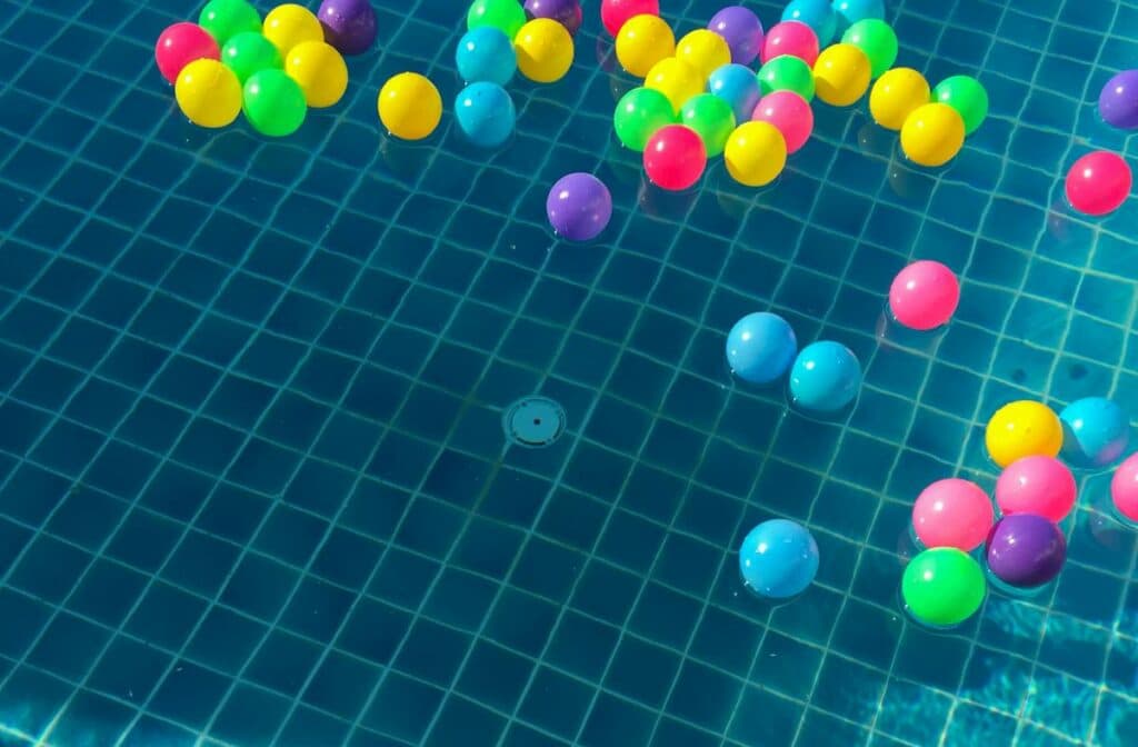 Floating colorful plastic balls in a sunlit swimming pool, creating a vibrant and playful scene.