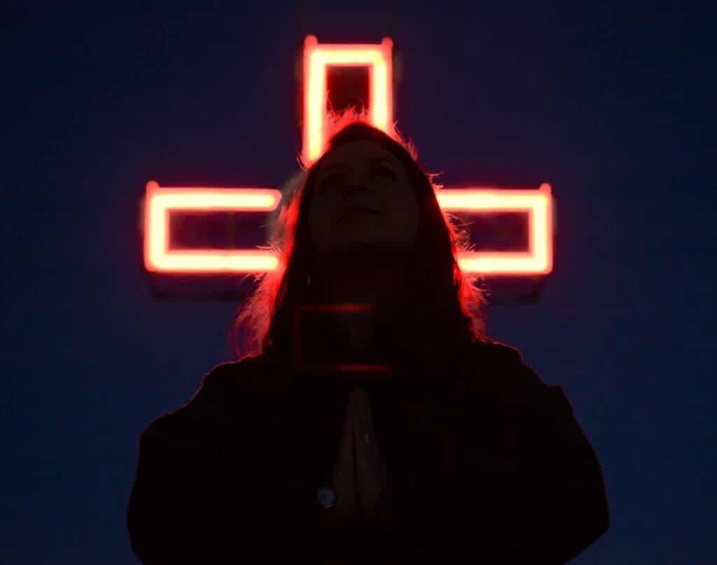 a woman standing in front of a lighted cross
