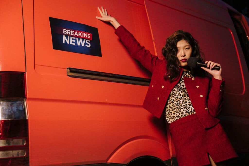 Fashionable reporter with microphone posing dramatically next to a news van.