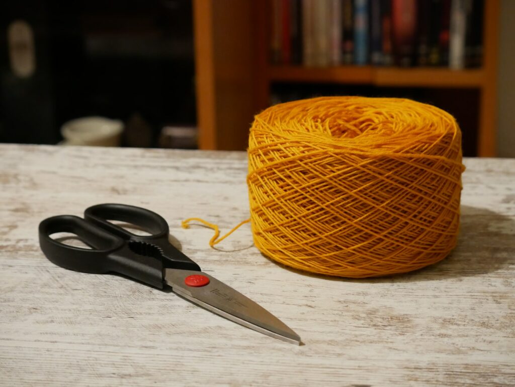 black handle scissors beside yellow yarn