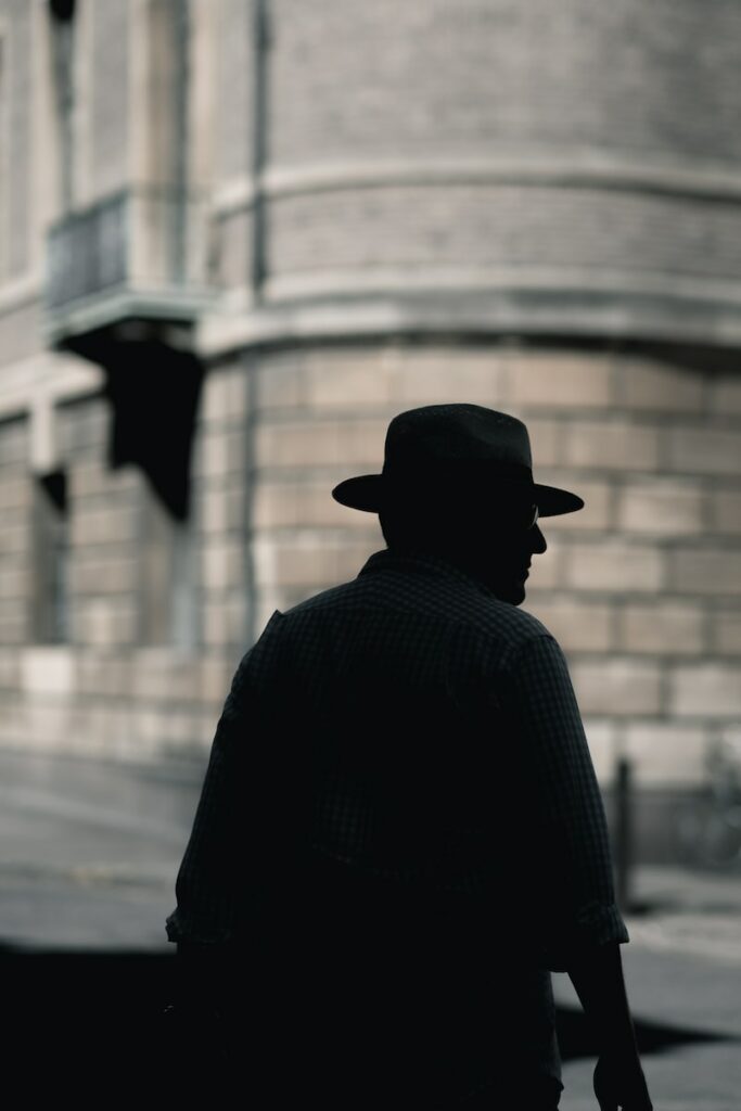 silhouette photo of a man with hat standing near concrete building at daytime