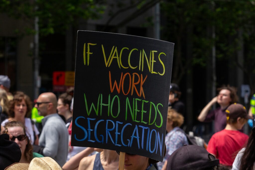 a person holding a sign that says if vaccines work who needs segre