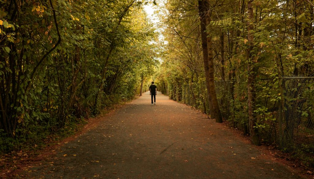 person in black jacket walking on pathway between trees during daytime